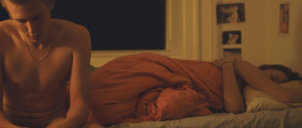 Image extraite du film Copenhague - A Love story de Philippe Lesage. On y voit un jeune homme assis sur le bord d'un lit, pensif. À ses côtés, une jeune femme sous la couette dort encore (courtoisie RVCQ)