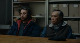 Les acteurs Mikael Gouin et Nguyen Thanh Tri sont accotés à une table en train d'écouter un interlocuteur que l'on ne voit pas (image extraite du film)