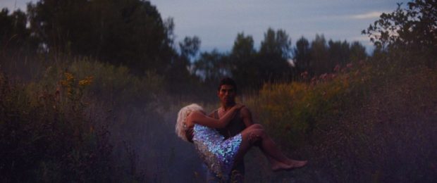 Un homme torse nu porte une jeune femme évanouie dans une clairière. Image extraite du film Les oiseaux ivres, de Ivan Grbovic.